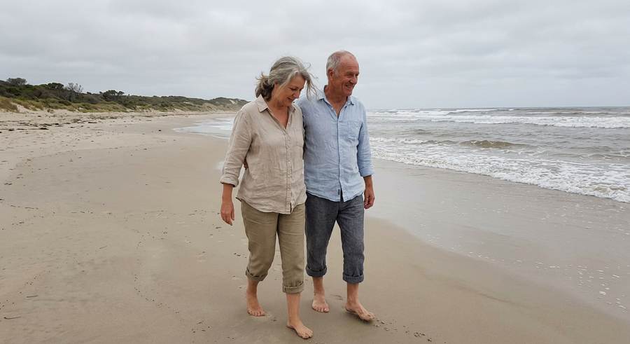 A couple in their late fifties walking on a beach on an overcast morning